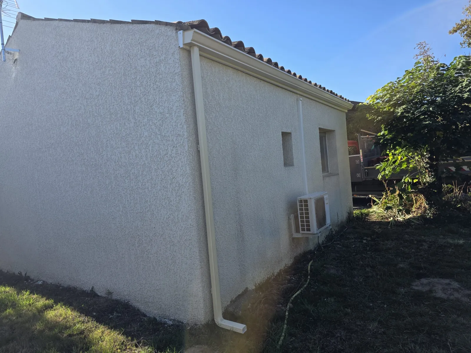 Façade en crépi avec gouttière et descente en aluminium blanc sous la toiture en tuiles