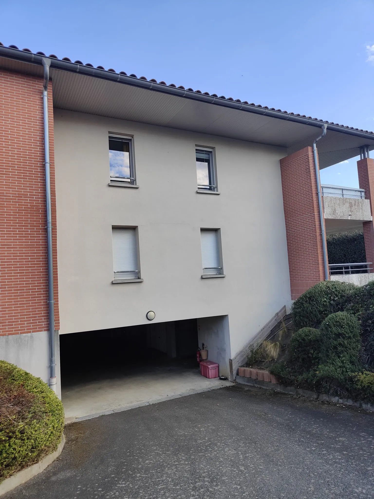 Après les travaux : Façade de l'immeuble en brique et enduit clair, débord de toit au-dessus de l'entrée du parking