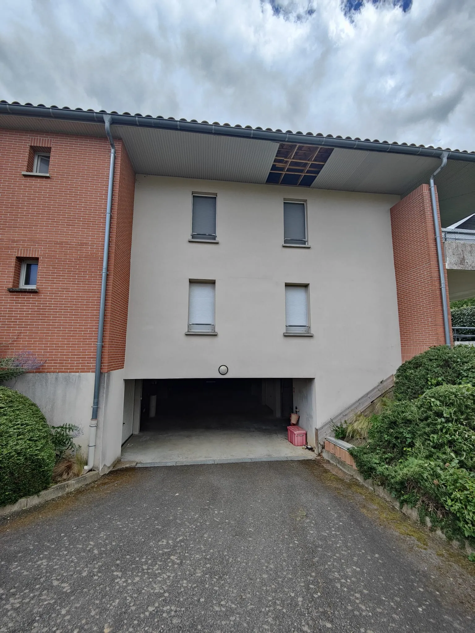 Avant les travaux : Façade de l'immeuble en brique et enduit clair, débord de toit au-dessus de l'entrée du parking