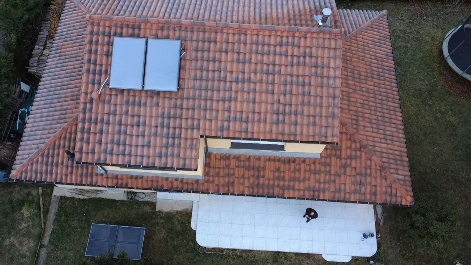 Vue rapprochée par drone d'une section de toiture en tuiles terre cuite montrant le faîtage, les noues et des panneaux solaires thermiques
