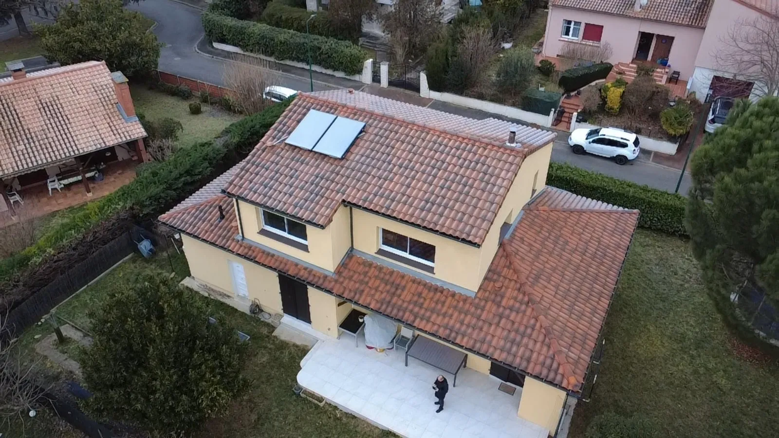 Vue aérienne par drone d'une maison toulousaine à étage avec toiture en tuiles terre cuite, panneaux solaires thermiques sur un pan et terrasse au sol