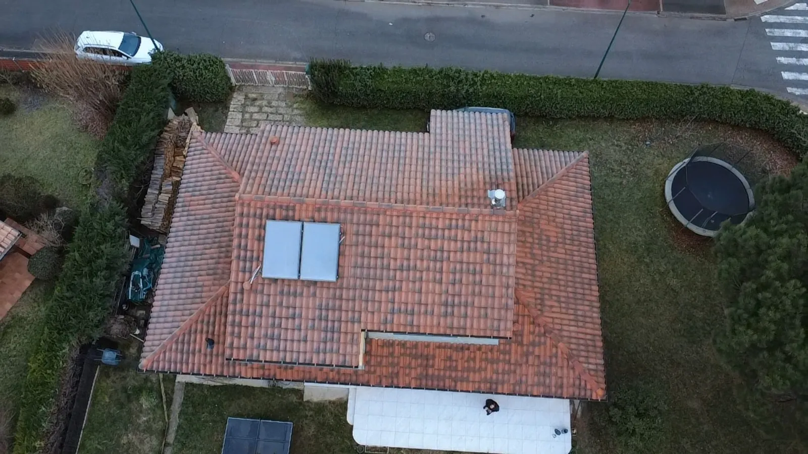 Vue zénithale par drone d'une couverture en tuiles terre cuite à pans multiples, avec faîtage, noues et panneaux solaires thermiques