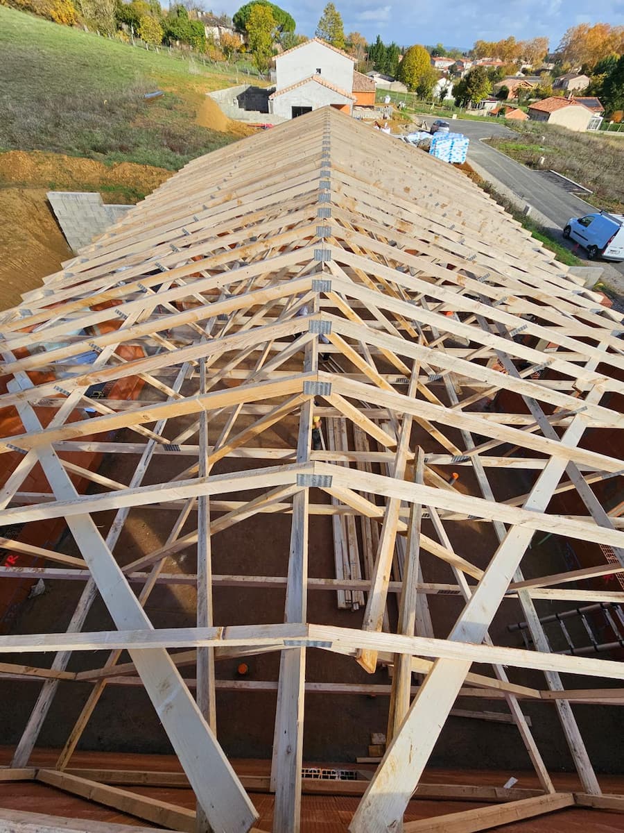 Charpente fermette industrielle, bois fins assemblés en triangles, sous une couverture en tuiles