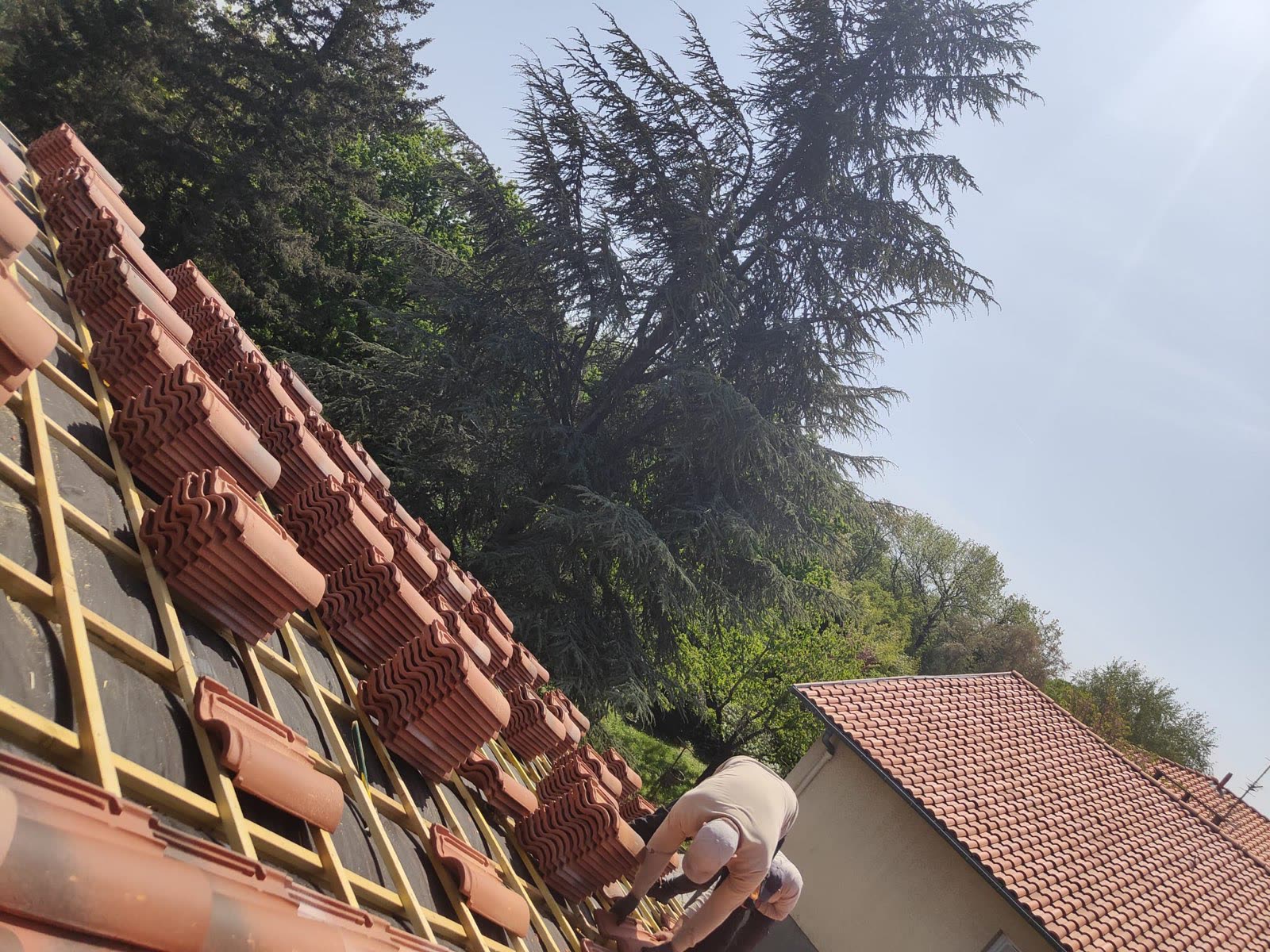 Pose de tuiles neuves le long du rampant lors d'une réfection de toiture par notre équipe