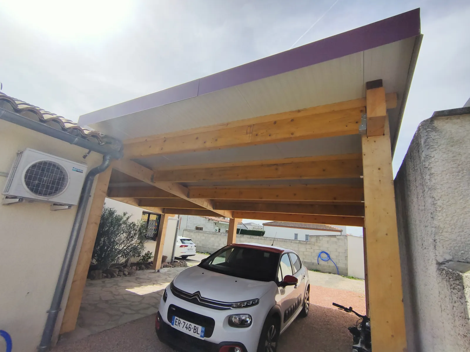 Vue en contre-plongée sous la charpente bois d'un carport à toit plat, poutres et poteaux en bois apparents