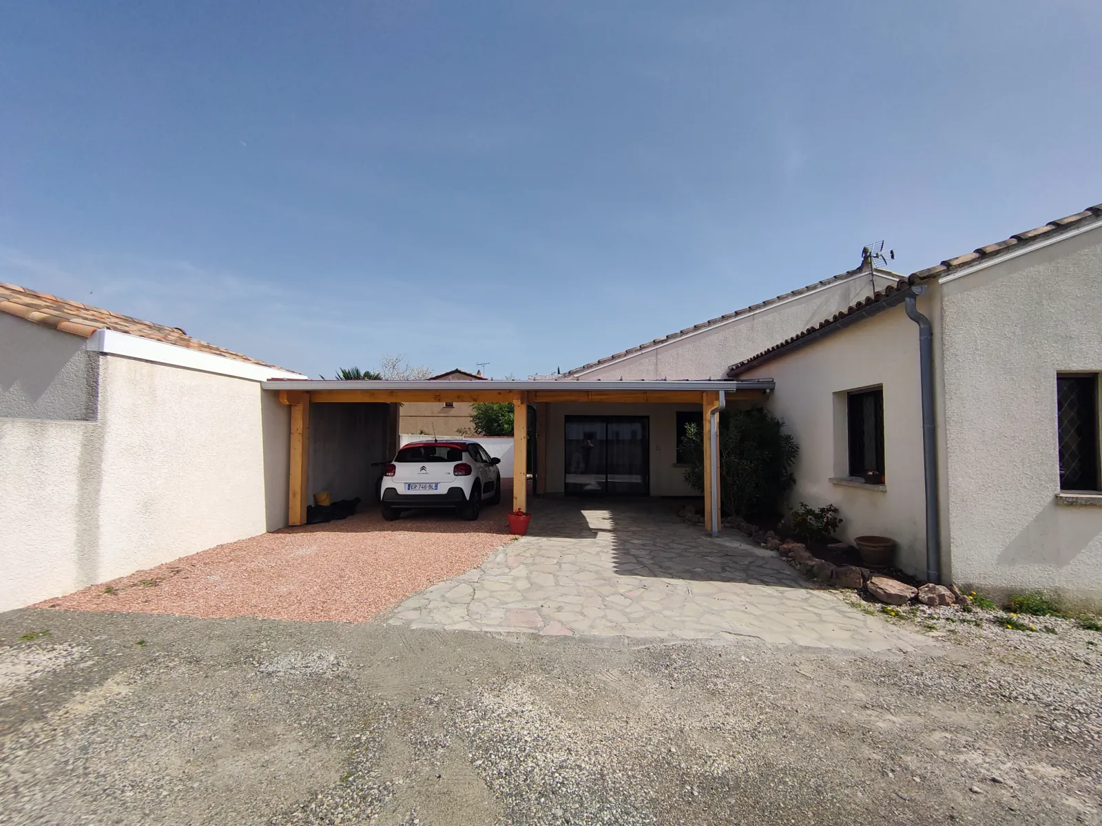 Carport en ossature bois adossé à une maison de plain-pied, vue d'ensemble depuis la cour