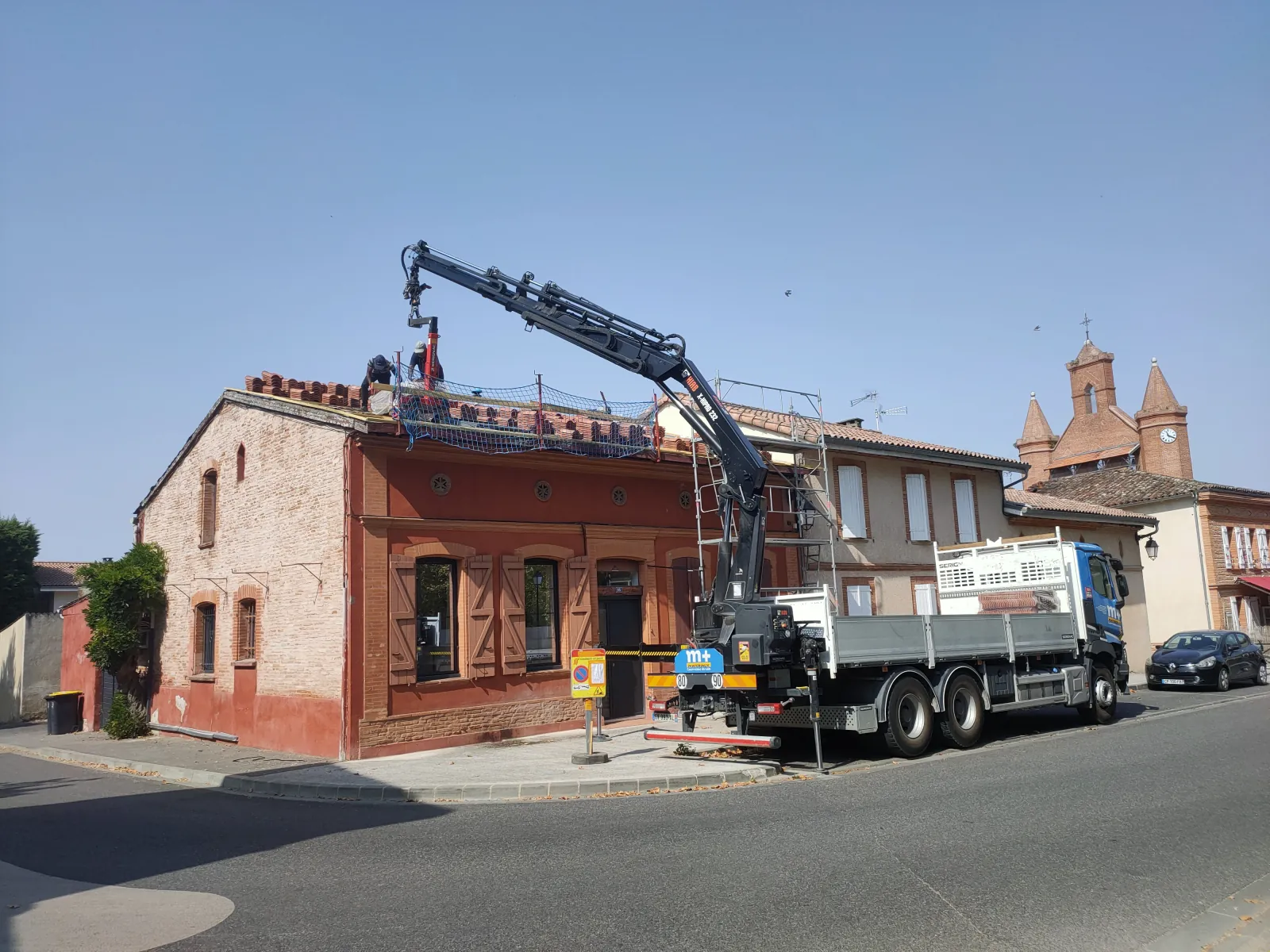 Chantier de rénovation de toiture sur maison ancienne en briques avec camion-grue, échafaudage et filet de sécurité