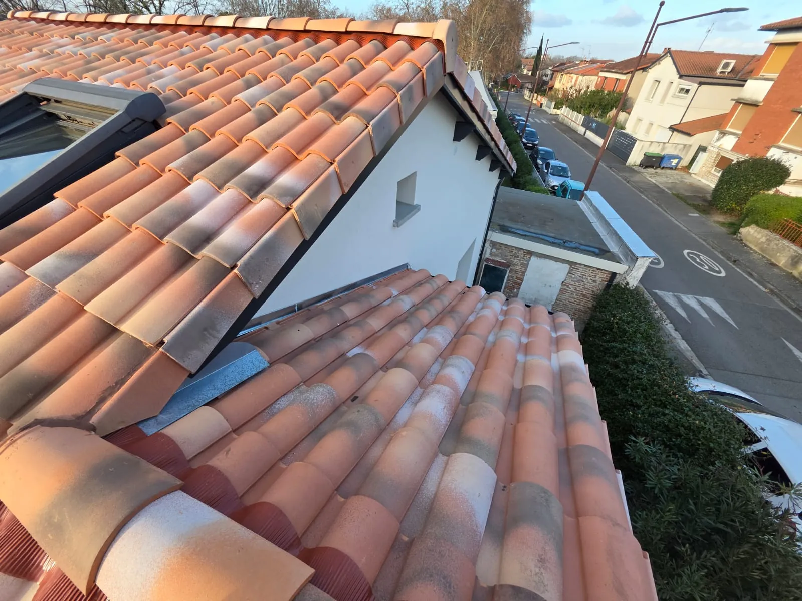Toiture en tuiles canal à deux pans avec fenêtre de toit, vue plongeante sur une rue résidentielle