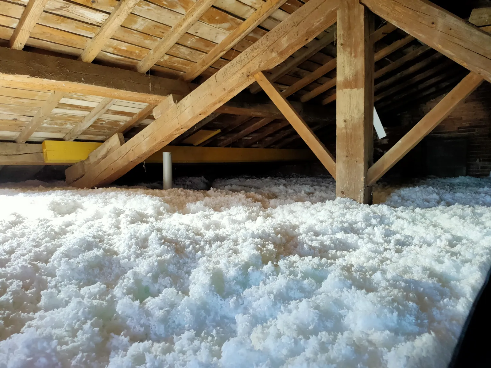 Comble perdu isolé par épaisse couche de laine soufflée blanche sous une charpente bois traditionnelle