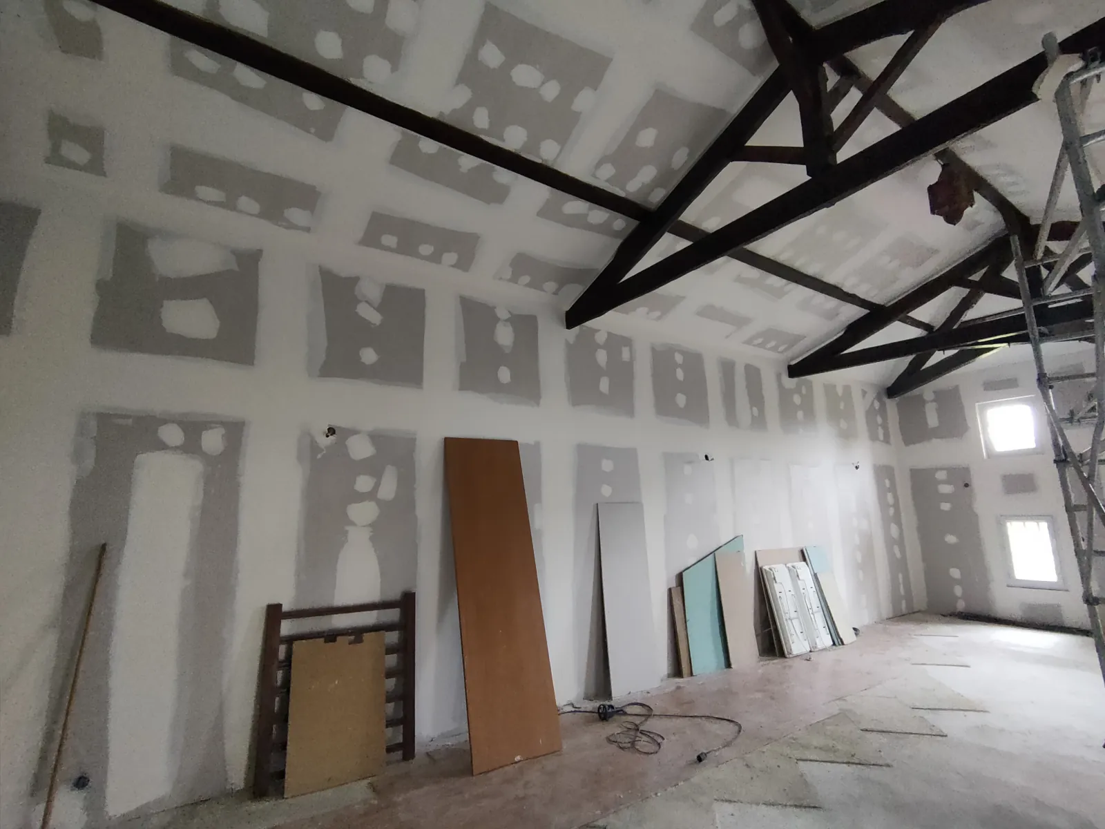 Comble aménagé en cours de rénovation avec plafond et murs en plaques de plâtre et charpente bois peinte apparente