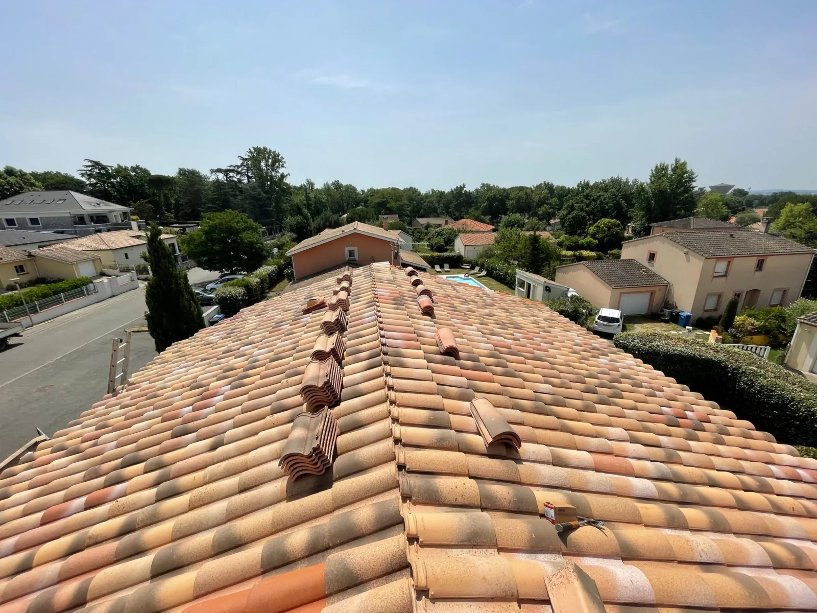 Toiture rénovée en tuiles canal terre cuite avec faîtière scellée, vue depuis le toit sur un quartier résidentiel
